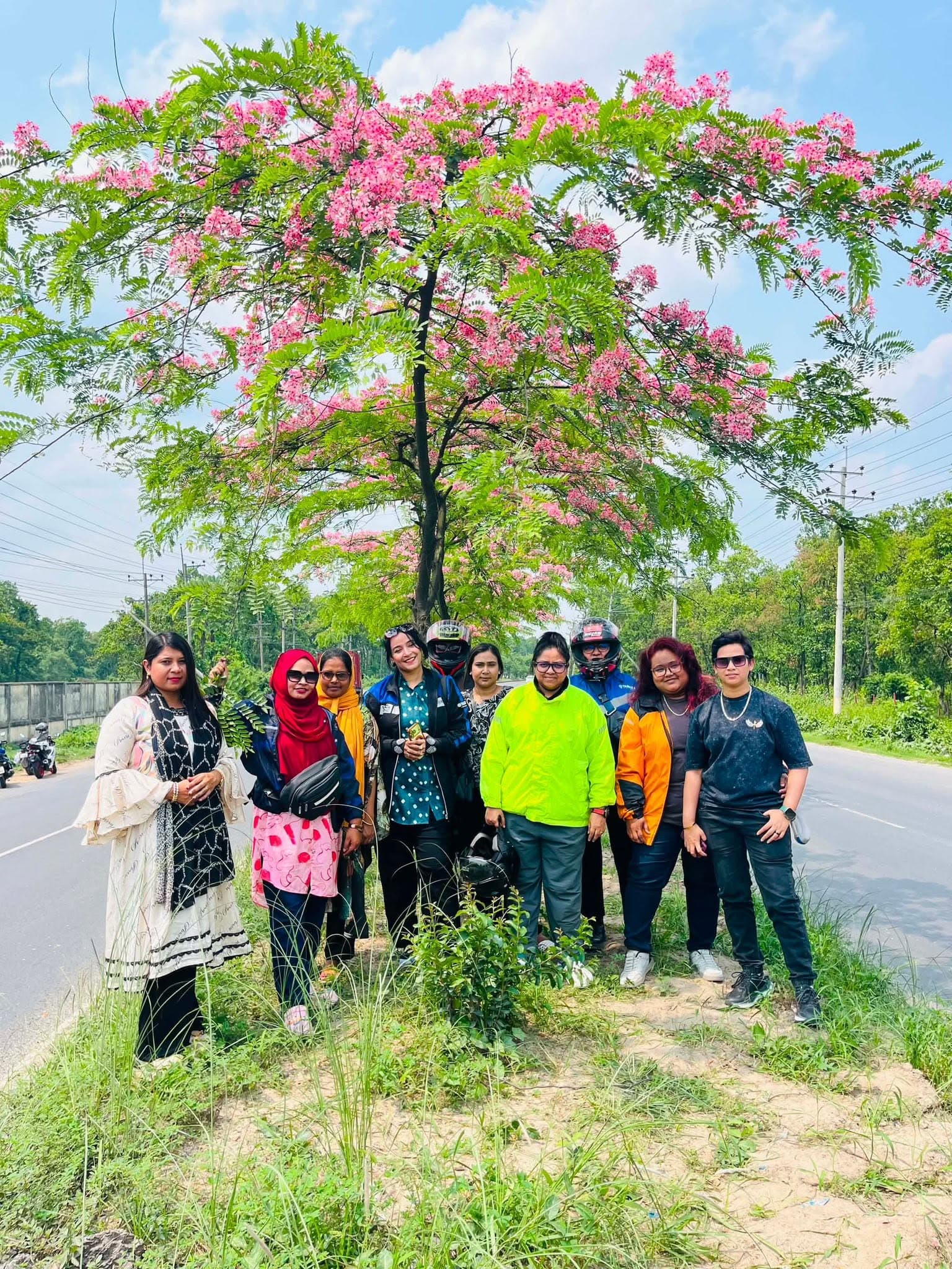 Bikers stopped on a group tour beside flowering trees.