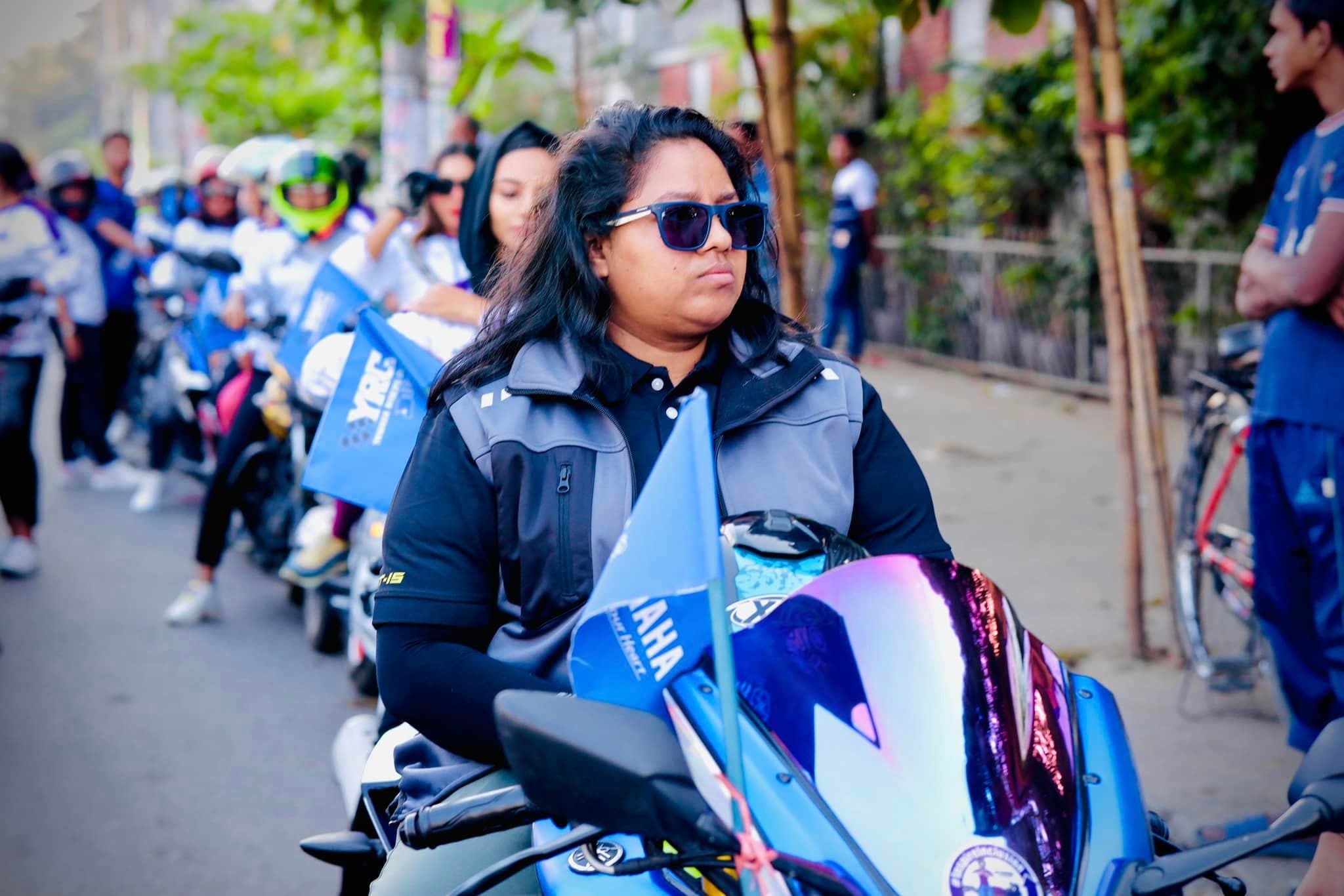 Portrait of Lina in sunglasses, seated on a blue Yamaha R15.
