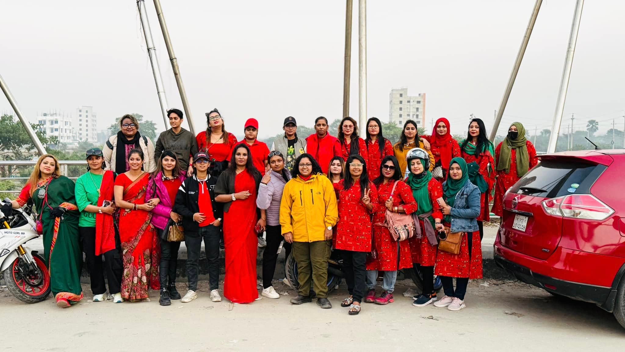 A large group of women dressed in red, standing with their bikes on a bridge.