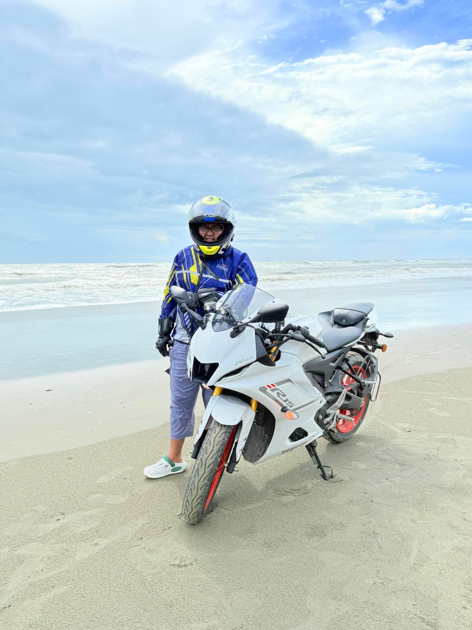 Lina standing with a Yamaha R15 on a beach. Portrait.